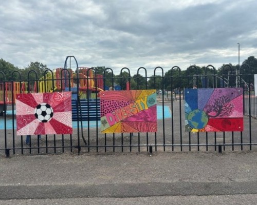 Three colourful murals attached to fencing, around a children's play park