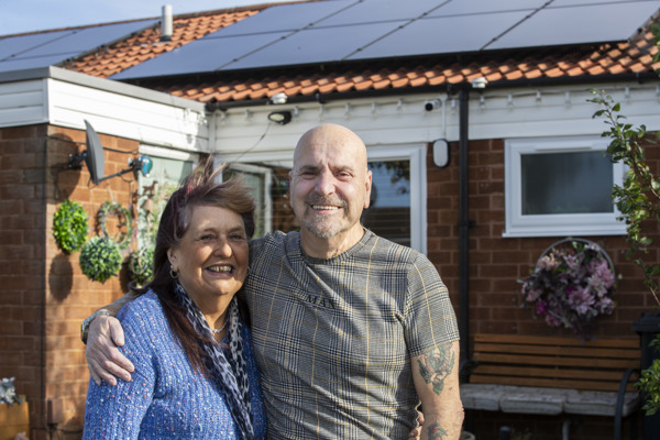 A happy couple in front of their home, which has been fitted with solar panels