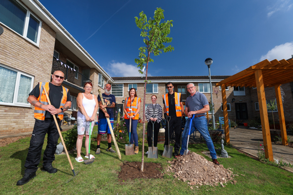 Thirteen staff and customers standing in communal garden with garden tools