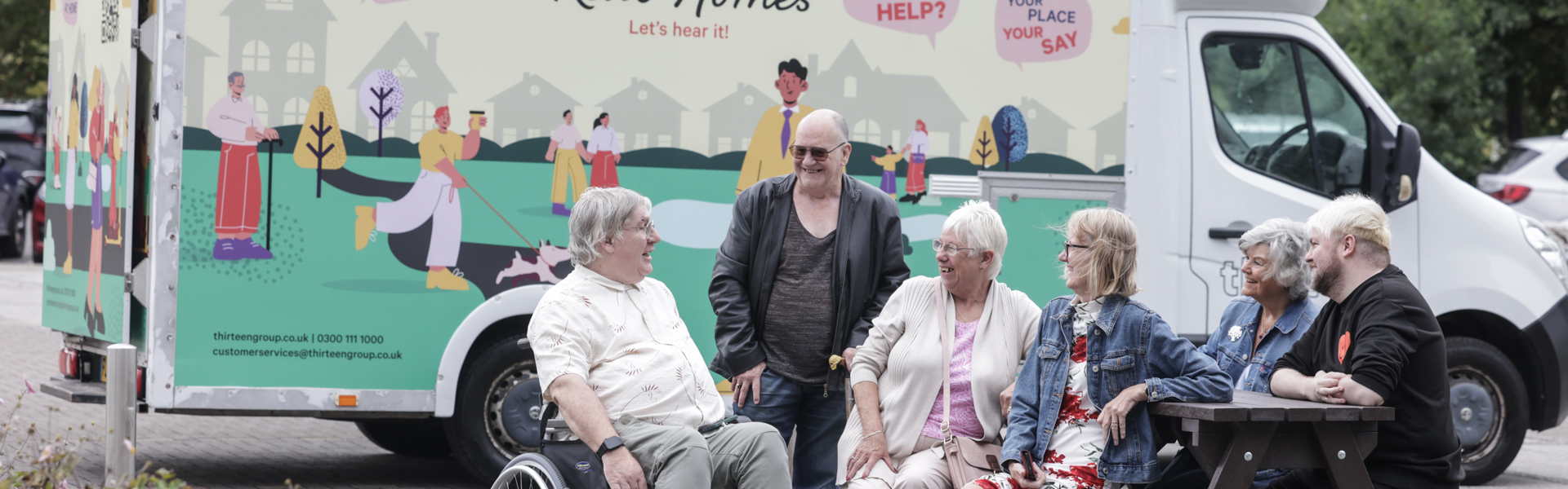 A group of residents, including a gentleman in a wheelchair, chat in front of Thriteen's mobile touchpoint van