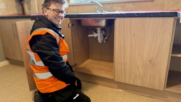 Plumbing apprentice Jessica Shaw kneeling in front of a sink's drainage system