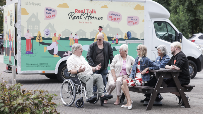 A group of customers are sat on a picnic bench talking in front of the mobile van