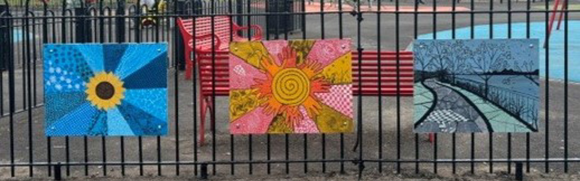 Three colourful murals attached to fencing, around a children's play park