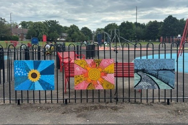 Three colourful murals attached to fencing, around a children's play park