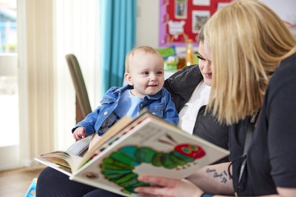 Baby girl smiles on woman's lap being read the very hungry caterpillar