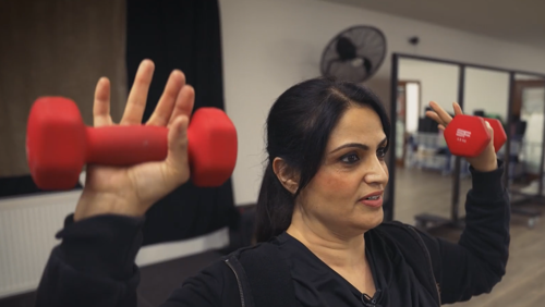 Close up of Shazia Noreen Ghani lifting two red dumbbells in a gym