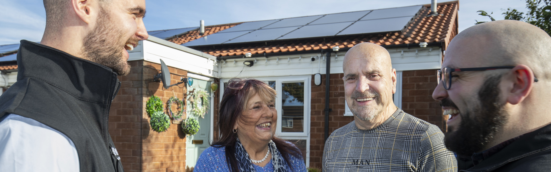 staff members with two customers showing solar panels on a bungalow