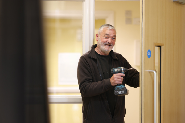 A Thirteen joiner with a drill, smiling through a fire door