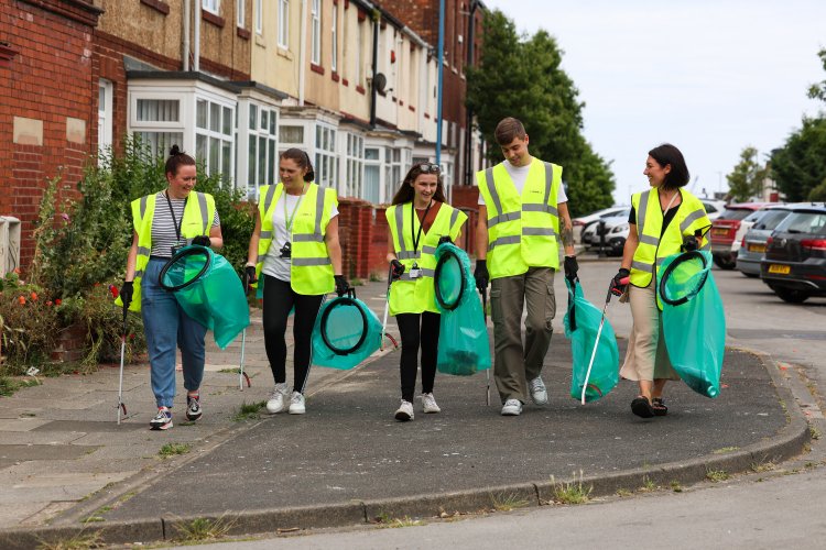 A team of thirteen colleagues walking on a street with litter pickers and rubbish bags